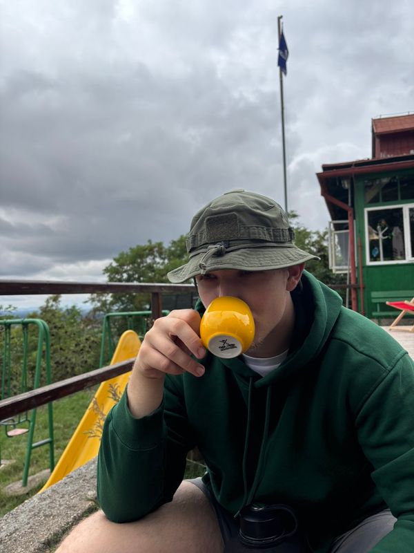 Robin Hrdlička v klobouku venku popíjí kávu z malého šálku